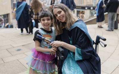 OU graduate Jade Ormiston wearing her graduation gown and with her child. 